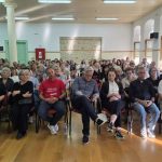 Μια σειρά από επίσημους προσκεκλημένους, συμπεριλαμβανομένου ενός ιερέα, καθισμένοι στην πρώτη σειρά του κοινού.