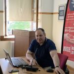 Ο ομιλητής, Δρ. Ιωάννης Σιάσιος, καθισμένος σε γραφείο μπροστά από λάπτοπ και μικρόφωνο, μιλάει στο ακροατήριο.